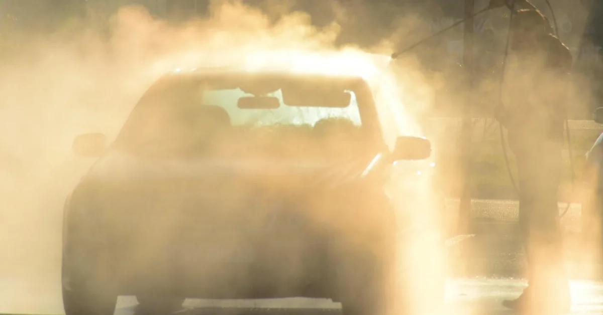 A car being washed outdoors with a spray wand in low sunlight