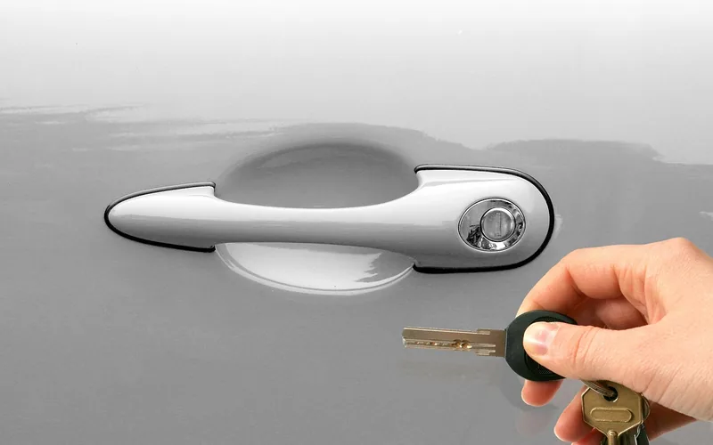 hand holding a car key beside a chrome exterior door handle hand holding a car key beside a chrome exterior door handle