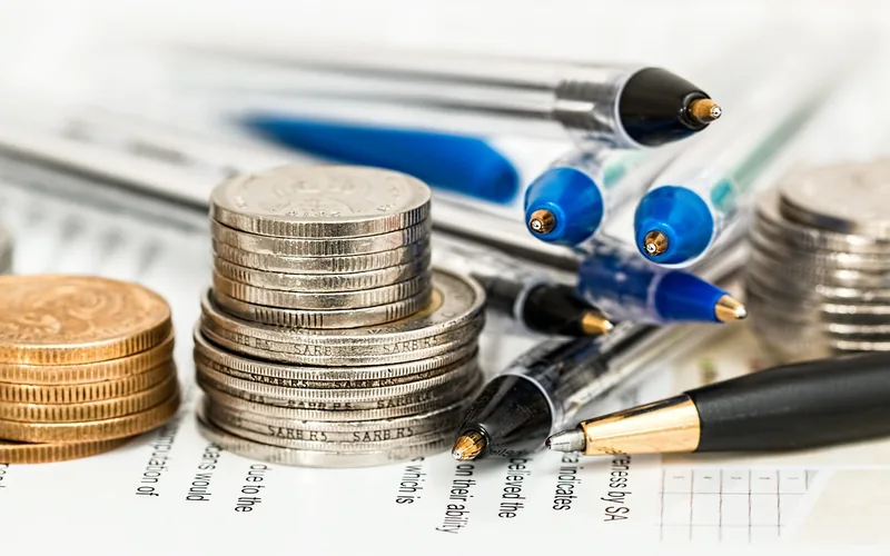 Calculating car repair insurance and vehicle service contract costs Stacked coins and pens on financial paperwork representing car repair insurance cost calculations