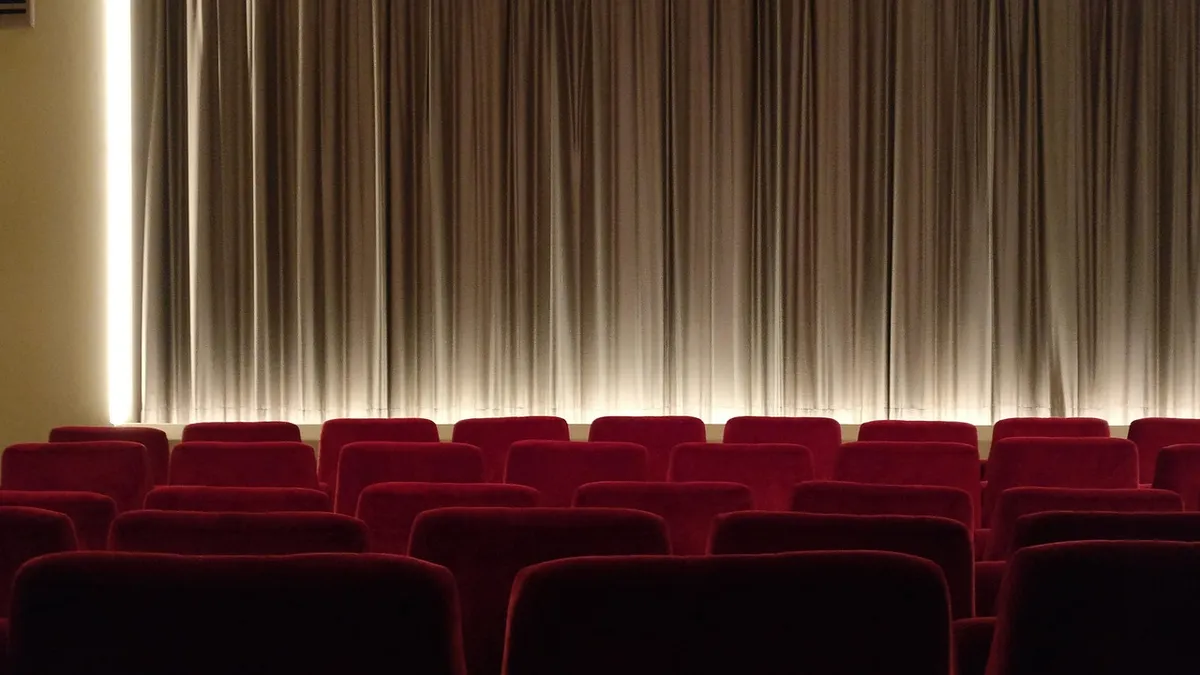Empty red cinema seats facing a lit screen curtain
