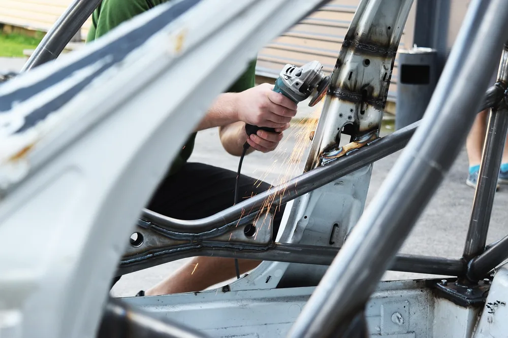 A worker grinds a welded seam on a bare car body shell