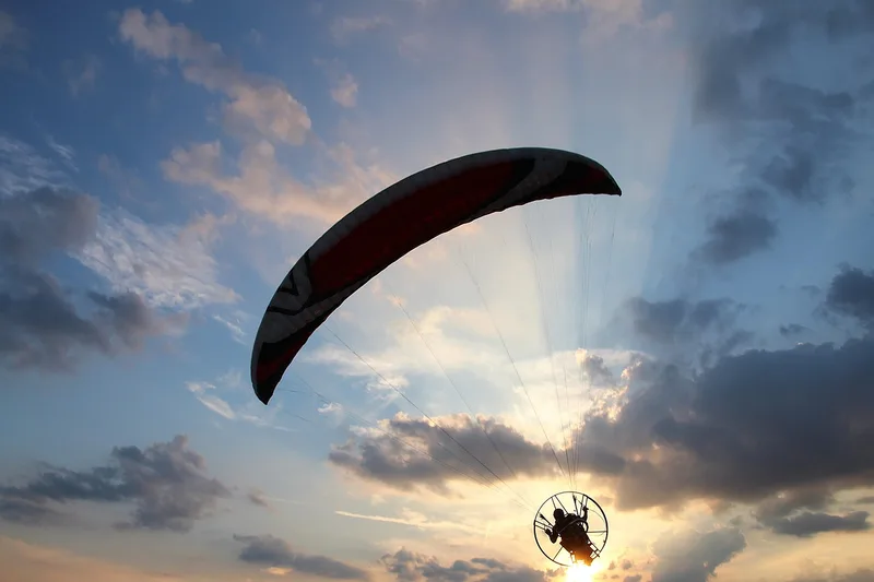 A paramotor pilot silhouetted against a evening sky