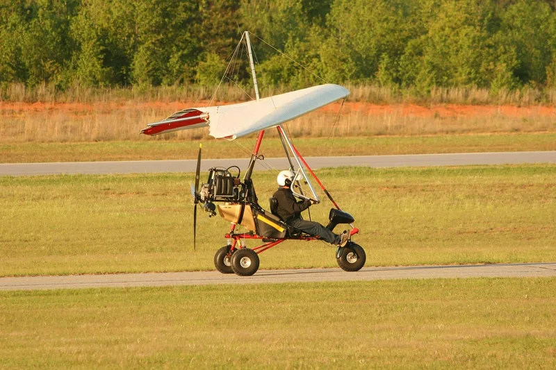 A single-seat powered trike aircraft with a pilot rolling along an airfield