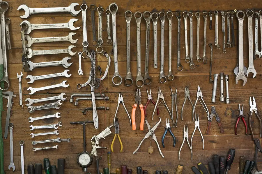 Wrenches, pliers and other hand tools hanging on a wooden garage wall