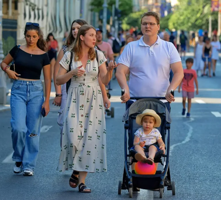 A family walking along a city street with a toddler riding in a stroller