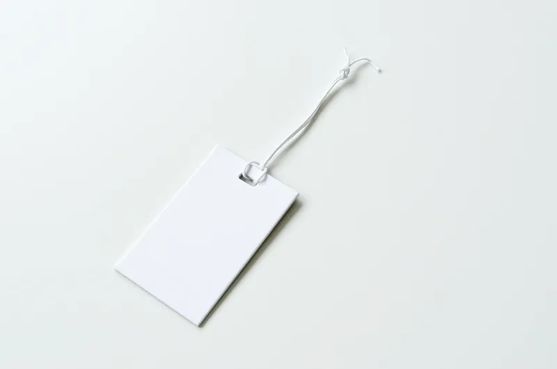 Blank white price tag on a string lying on a white surface