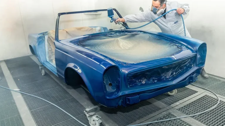 Painter wearing a respirator spraying a car body in a paint booth