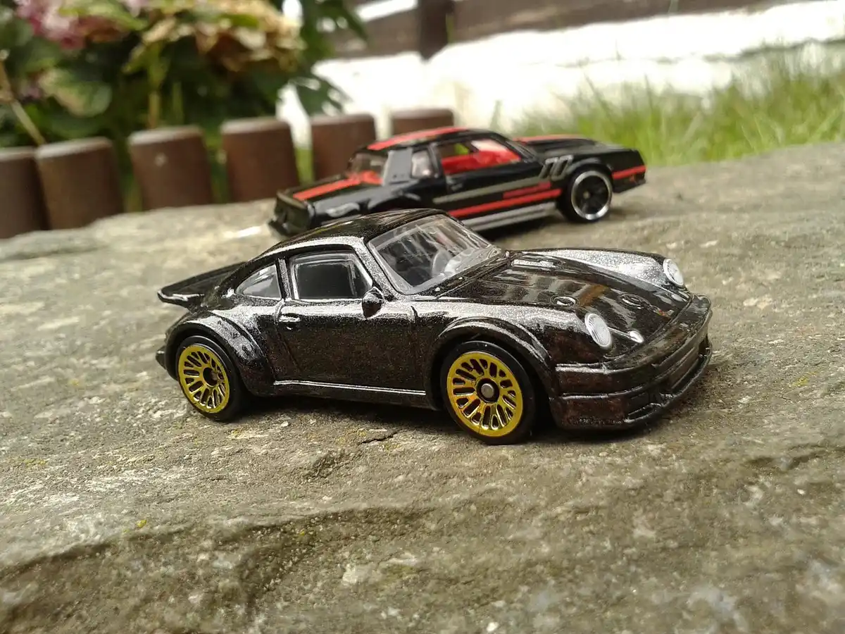 Two small black die-cast toy cars on a stone surface outdoors