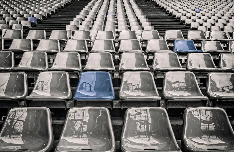 Rows of empty grandstand seats in grey tones with a few blue seats