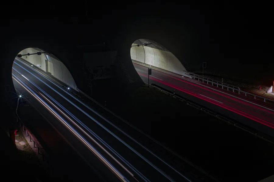 Night long-exposure photo of highway traffic leaving two tunnel portals