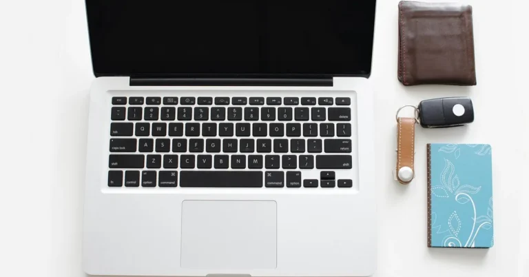 Laptop, brown wallet and a car key laid out on a white desk