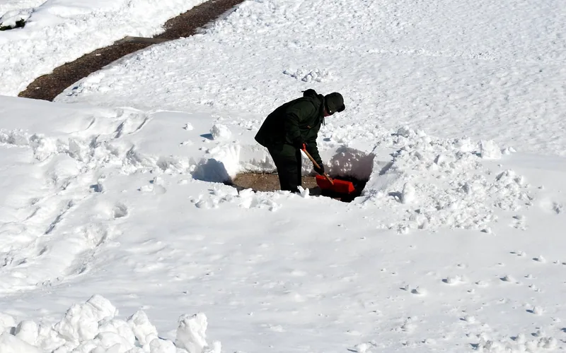 Man shoveling snow outdoors in cold winter weather wearing warm clothing Man shoveling snow outdoors in cold winter weather wearing warm clothing