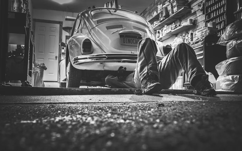 mechanic lying underneath a car raised for underside access in a home garage