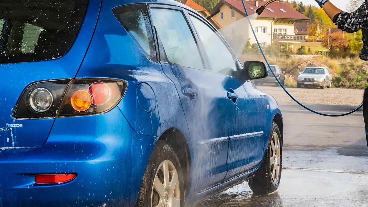 Car passing through an automatic exterior wash tunnel with soap and brushes, similar to a Mister Car Wash express wash