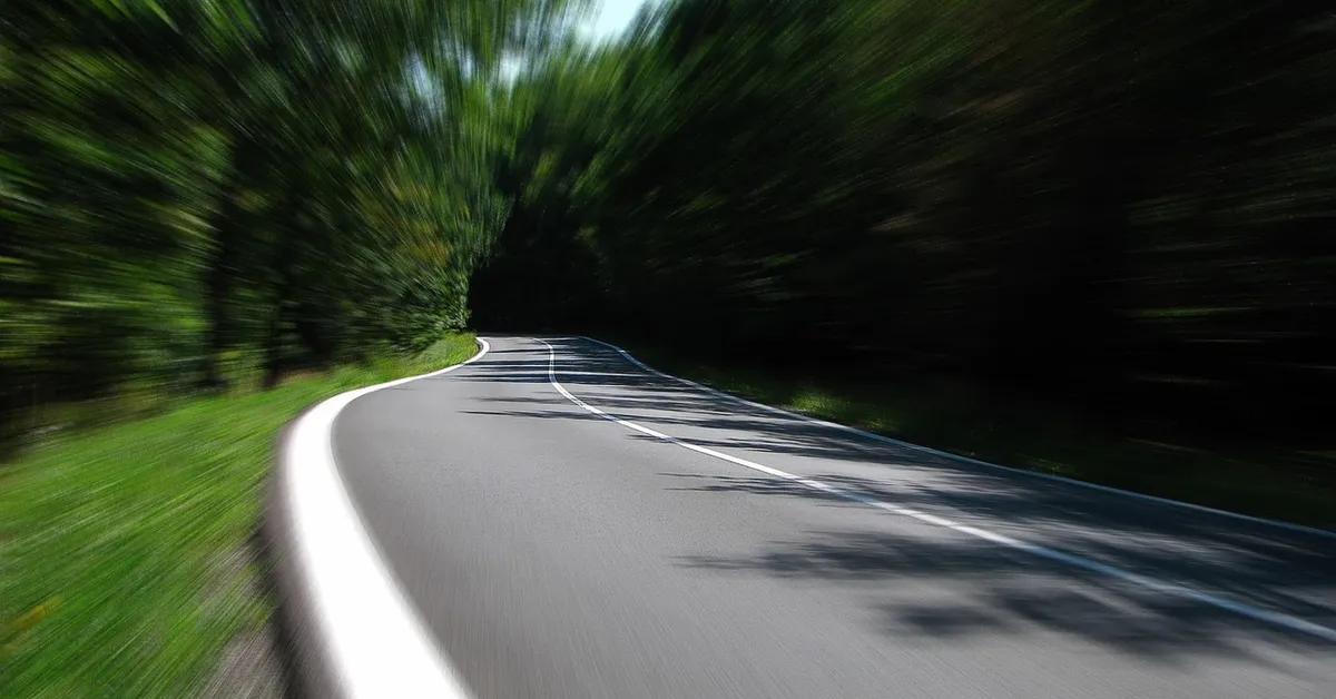 Motion-blurred curving road through green trees