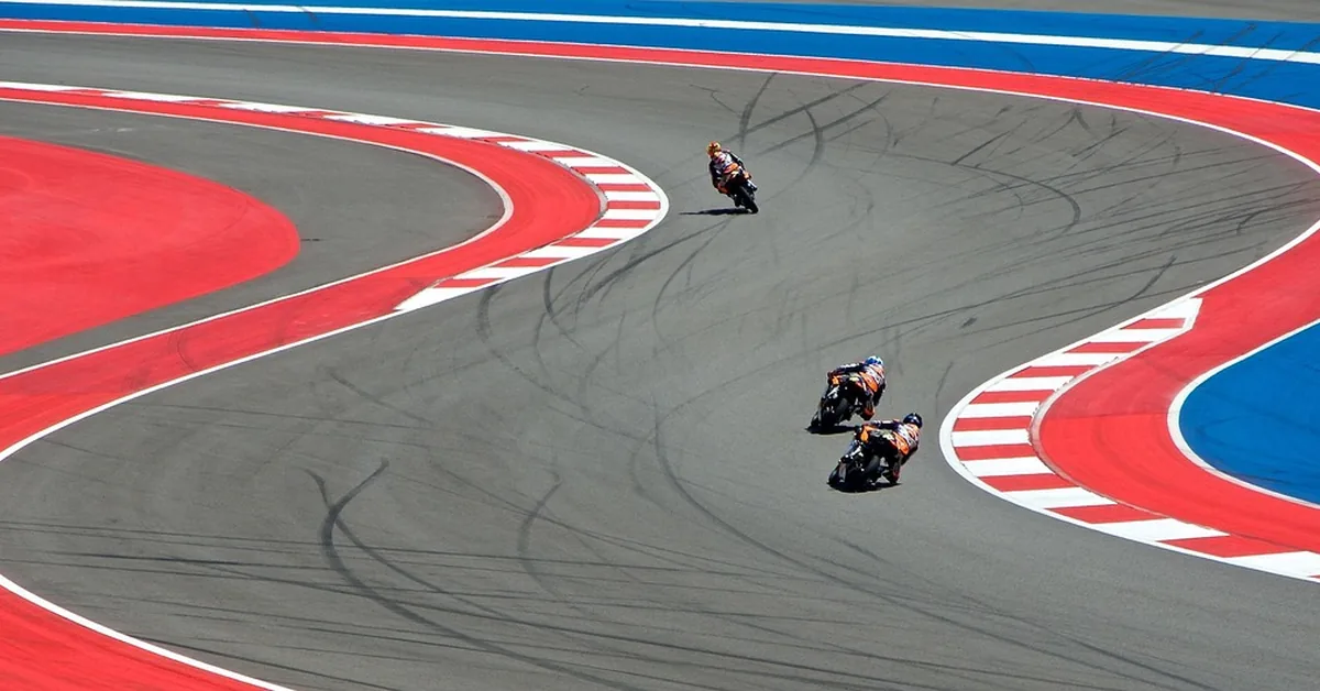 Riders taking a corner on a road-racing circuit with red and white kerbs
