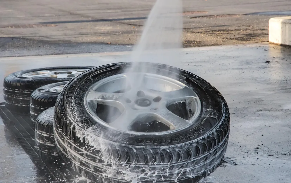 Water rinsing soap suds off a car wheel and tire on wet pavement