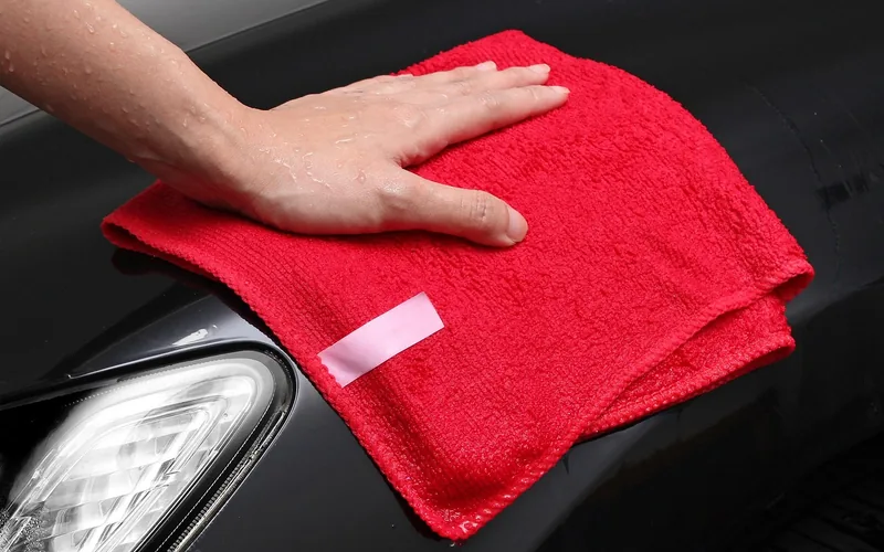 microfiber cloth wiping diluted rubbing alcohol off a red car's painted panel