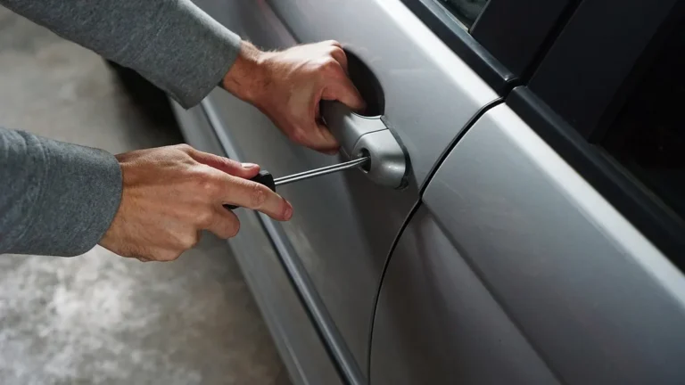 Hands forcing a car door lock with a screwdriver