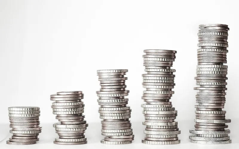 Five stacks of coins in rising heights on a white surface