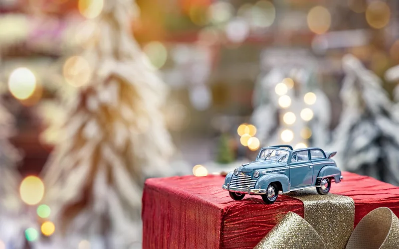 Small toy car on a red gift box with blurred lights behind