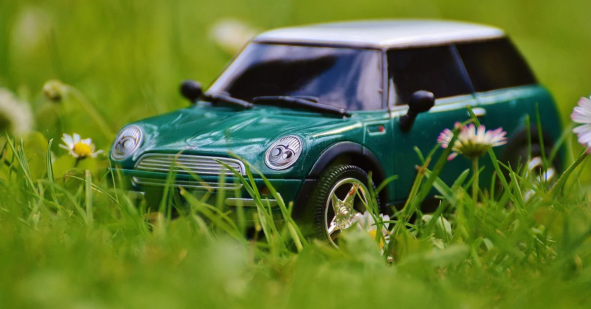 Small green toy car parked in grass among daisies, a stand-in for a new car purchase