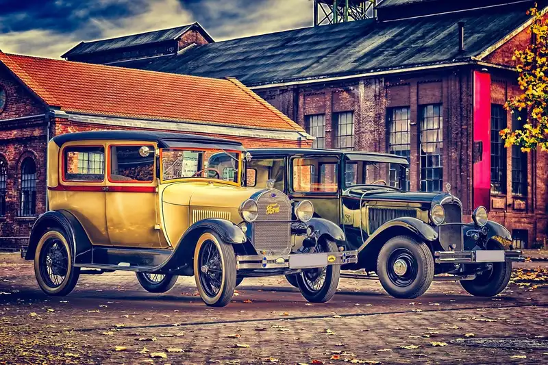 Two antique cars parked outside a brick industrial building