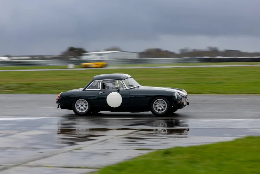 Dark green vintage sports coupe driving on a wet race circuit