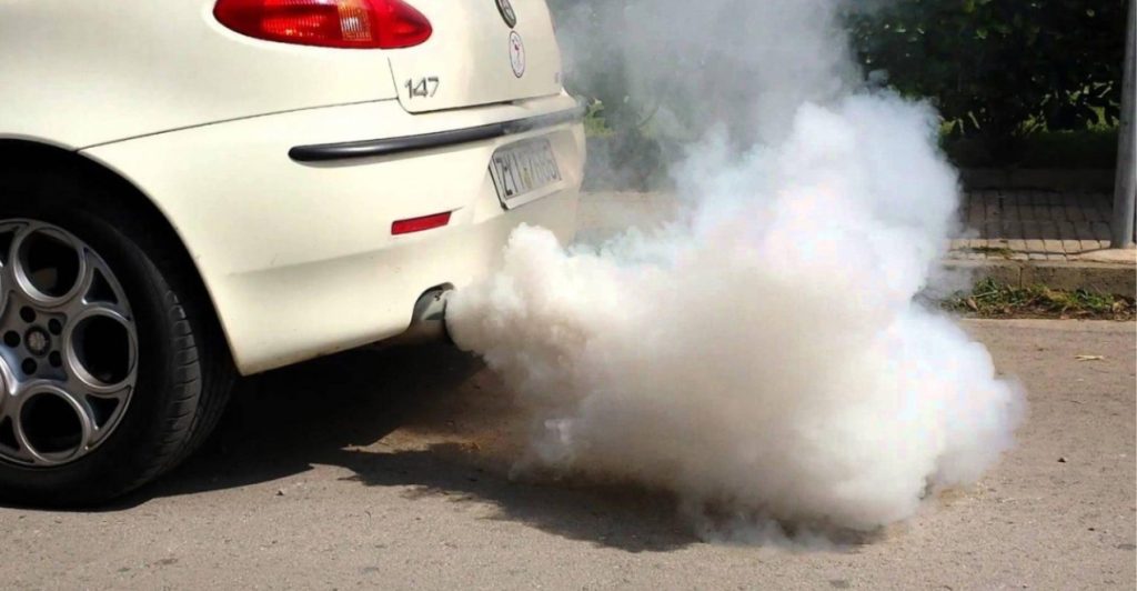 White smoke billowing from the exhaust pipe of a car parked on a driveway