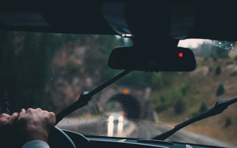 Windshield wiper blades and a driver's hand on the steering wheel seen from inside a car