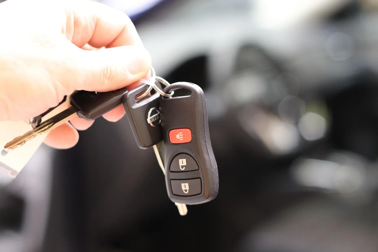 Hand holding a basic metal car key and a transponder key fob with buttons Hand holding a basic metal car key and a transponder key fob with buttons