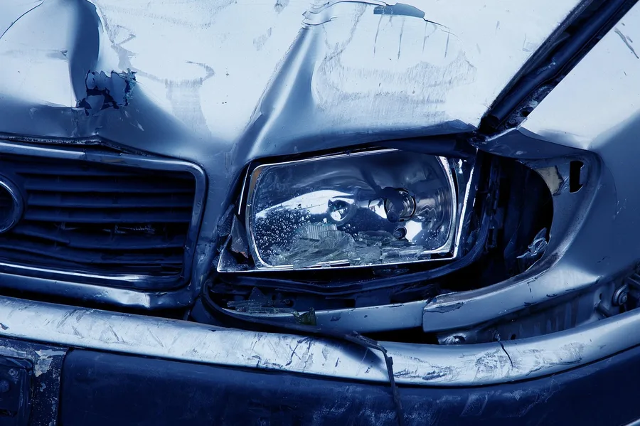 Close-up of a car's crumpled front-end structure after a collision, showing bent metal near the headlight