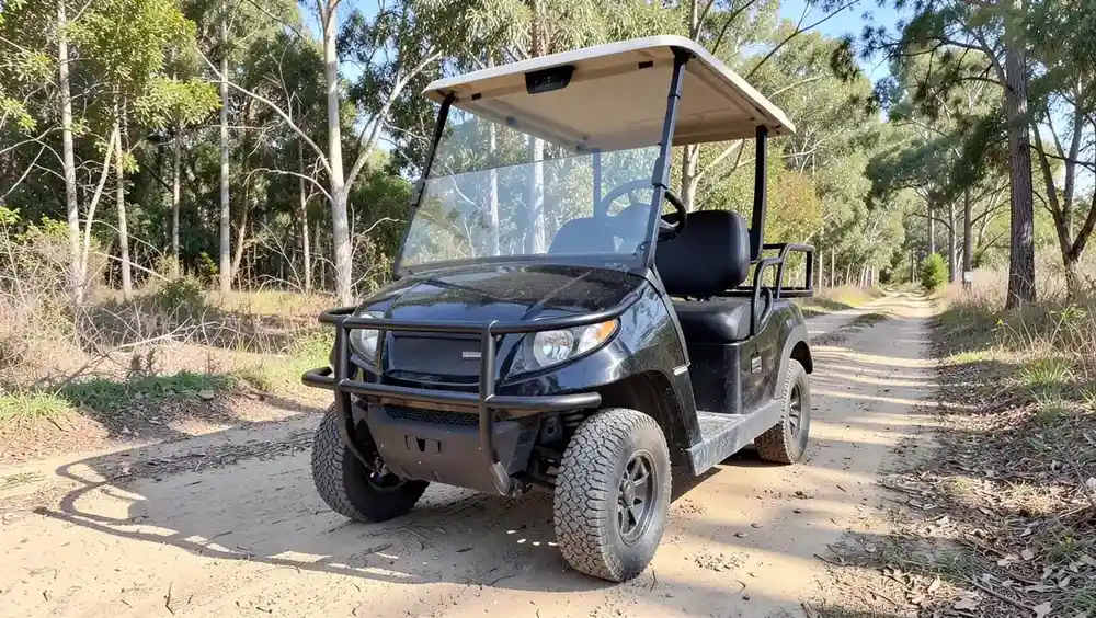 Black golf cart with a tubular steel brush guard bumper mounted on the front, parked on a dirt trail