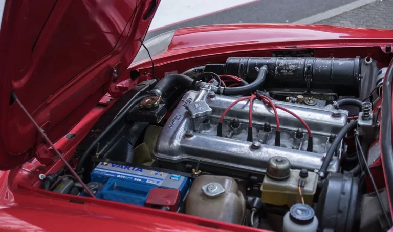 Open hood of a red car showing the engine bay with the battery at the lower left