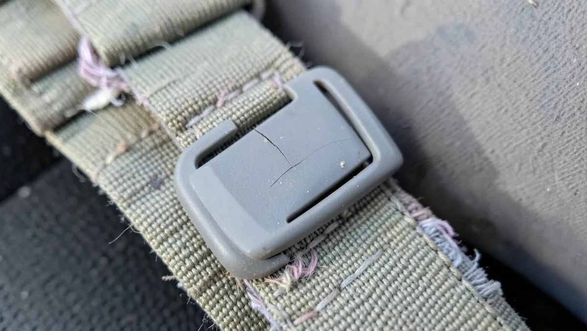 Close-up of a sun-faded, frayed car seat harness strap with a hairline crack in the plastic buckle clip