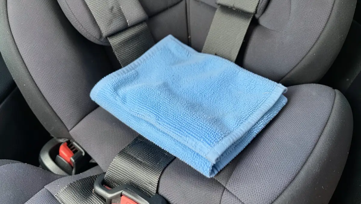 A folded microfiber cloth resting on the fabric cover of a child car seat for routine cleaning