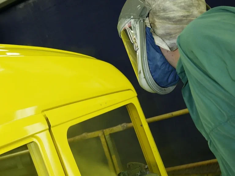 Painter in a respirator hood spraying yellow paint on a vehicle cab