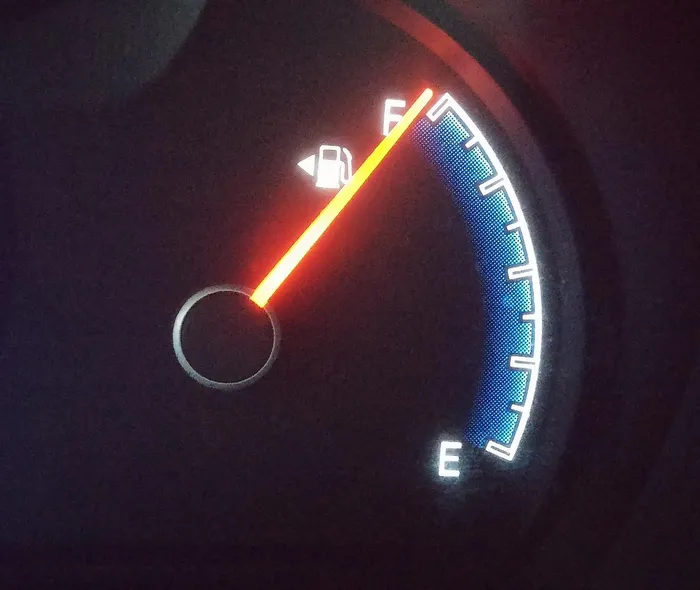 Dashboard fuel gauge needle near empty with the low fuel warning light lit