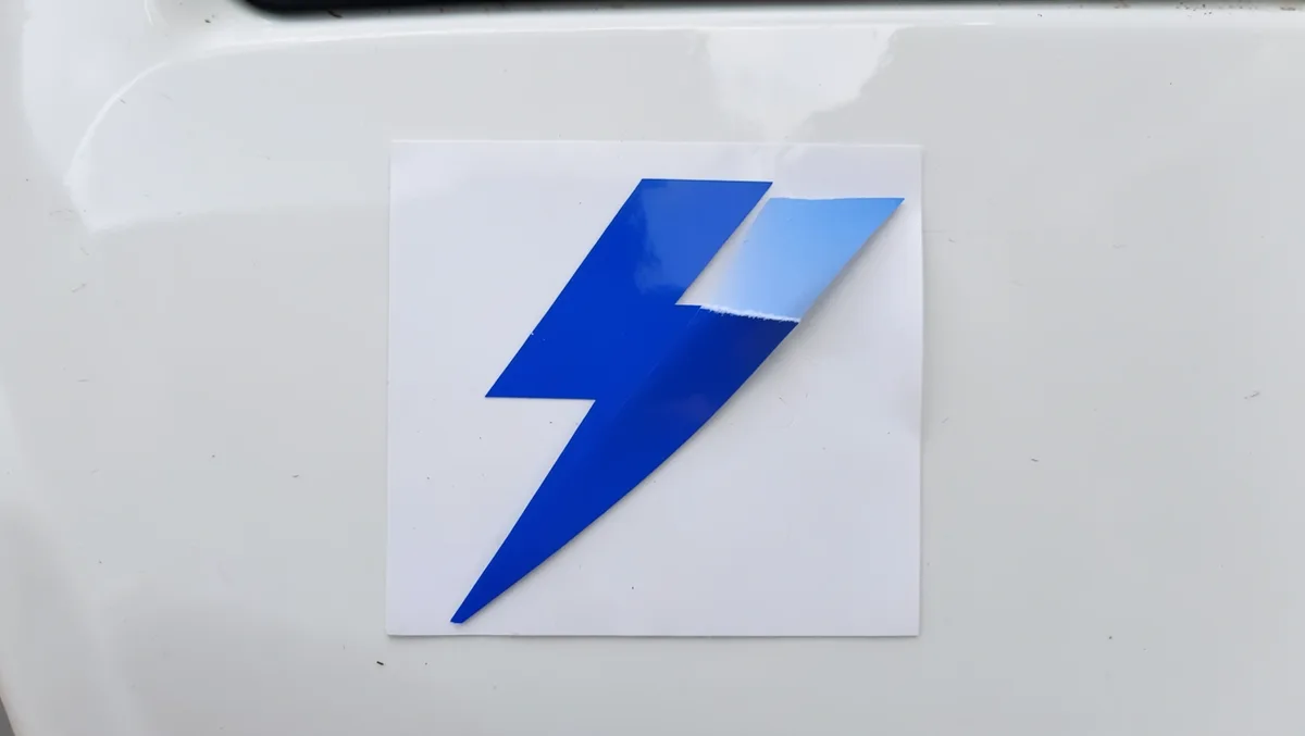 Blue lightning bolt vinyl decal half-peeled from its backing paper on a white car door panel