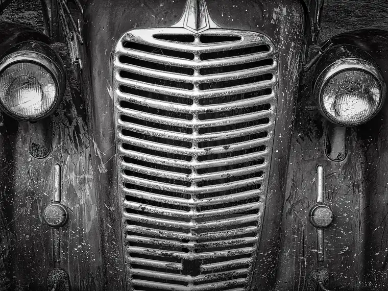 Weathered chrome front grille and round headlights of an older vehicle in black and white