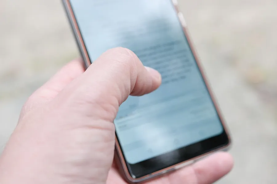 Hand holding a smartphone and touching the screen outdoors