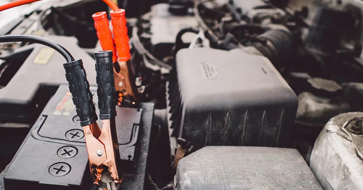 Red and black battery clamps attached to a car battery in an engine bay