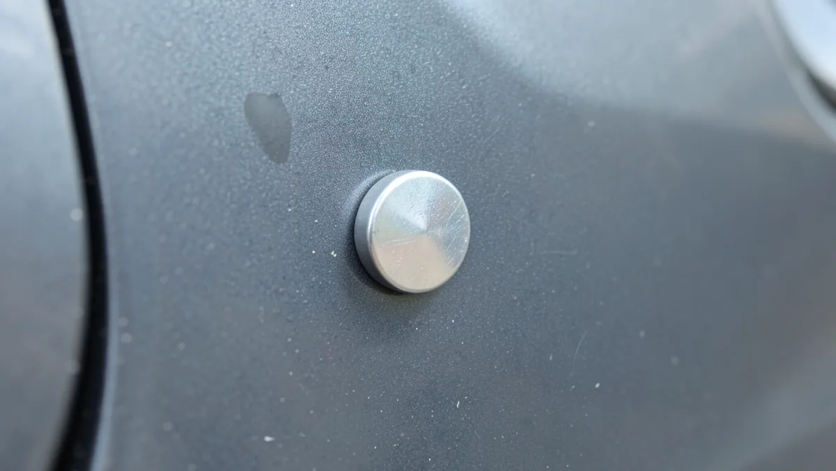 Small magnet stuck flush against a car door panel to test if the metal is magnetic