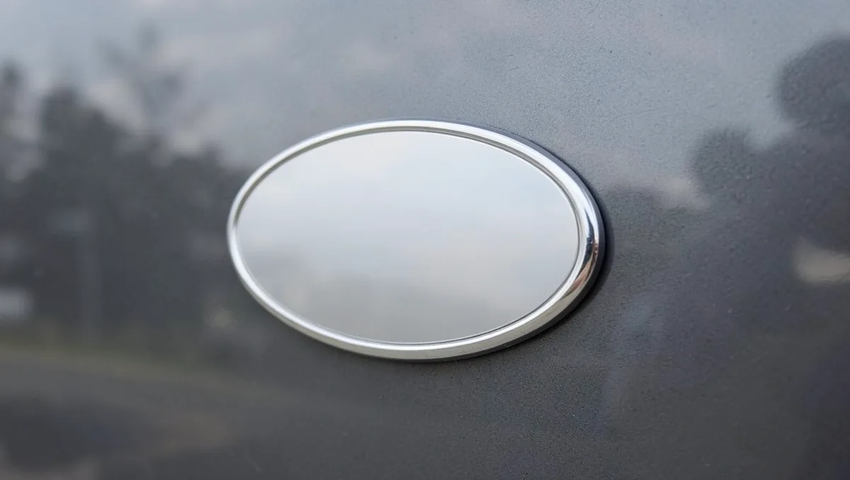 Blank chrome oval emblem mounted on a truck tailgate, representing a metal car emblem before a badge design is applied