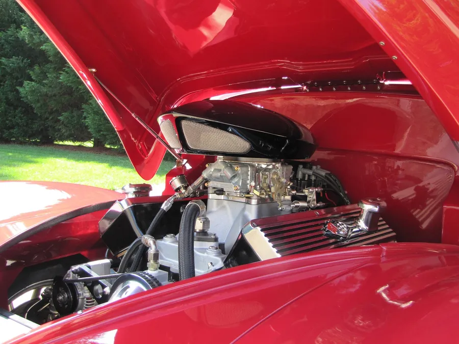 Open hood of a red hot rod showing a chrome carbureted engine