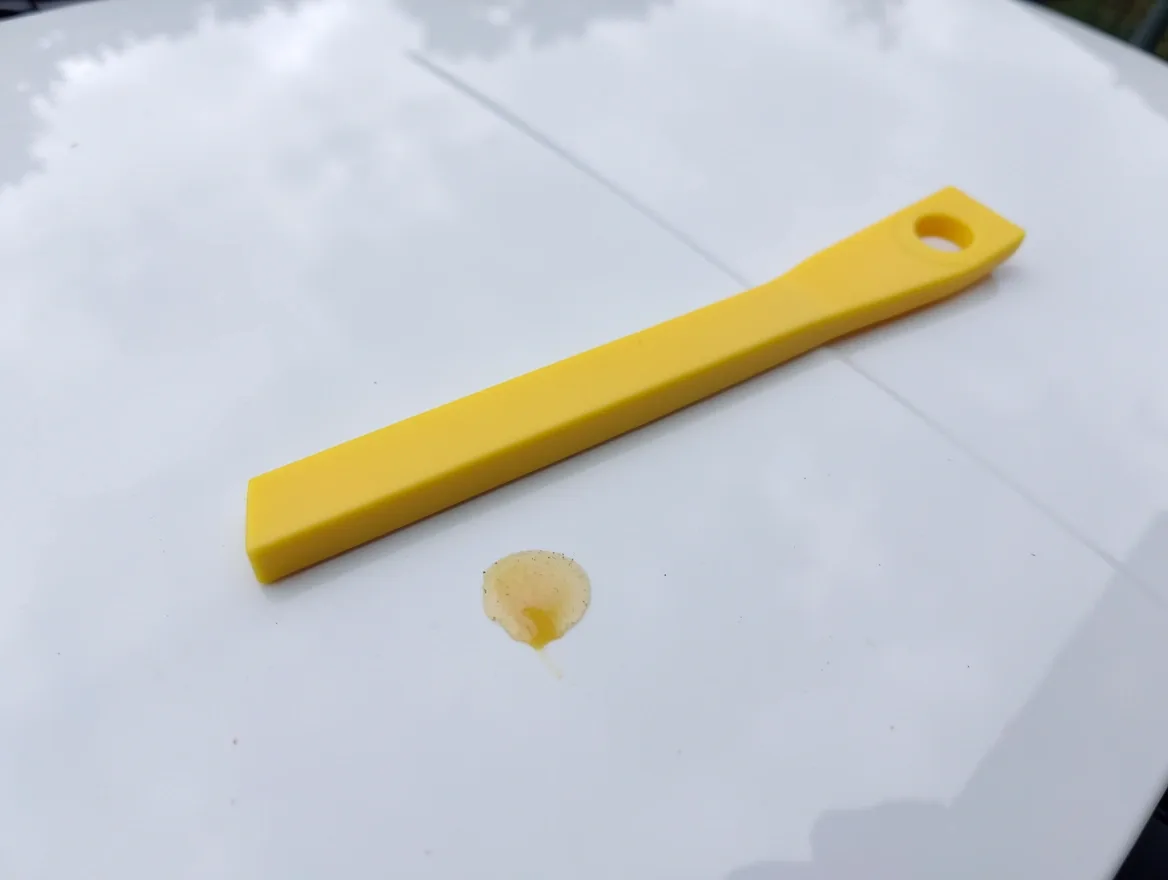 plastic scraper tool next to gum residue on a car hood