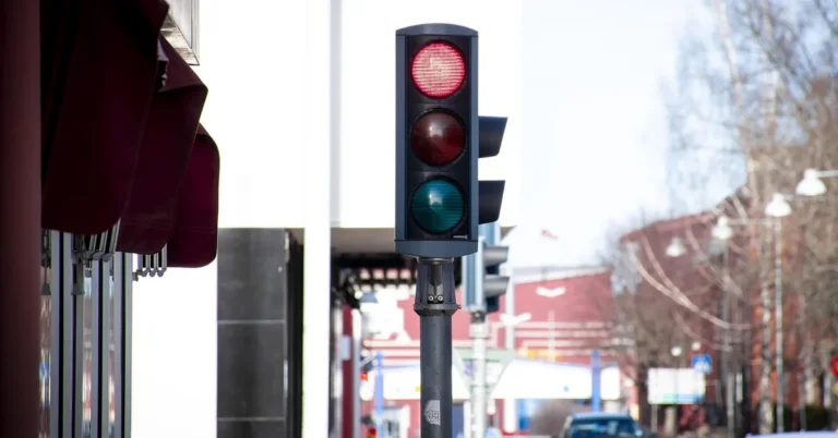 Red traffic light on a city street with a car approaching in the distance