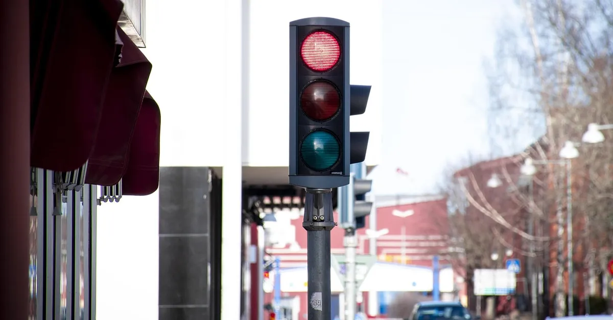 Red traffic light on a city street with a car approaching in the distance