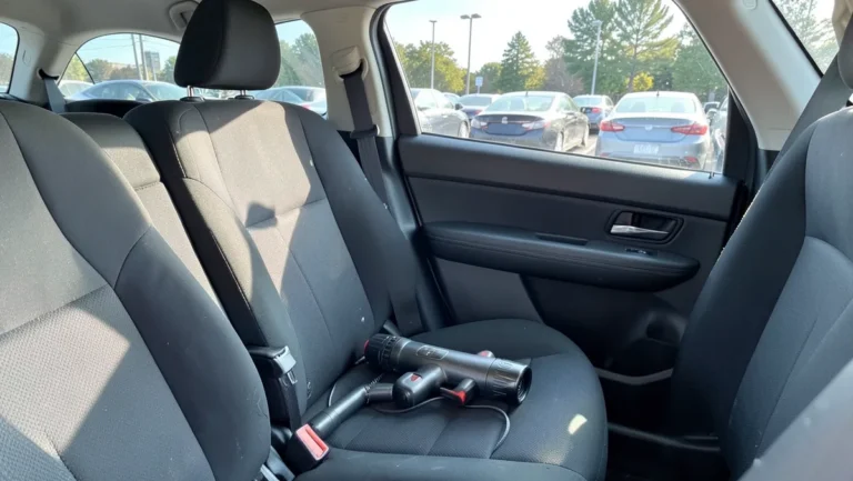 Cordless handheld vacuum resting on the back seat of a rental car with the parking lot visible through the window