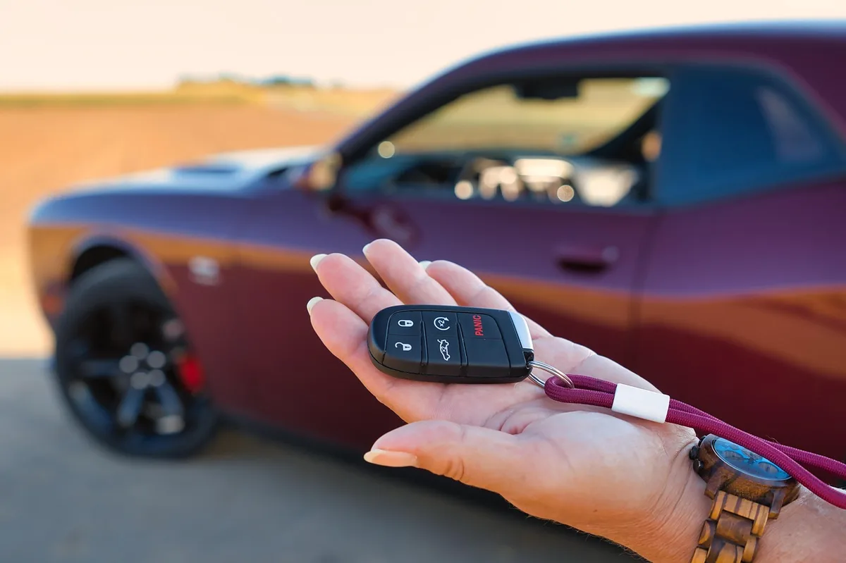 Hand holding a car key fob near a vehicle door handle